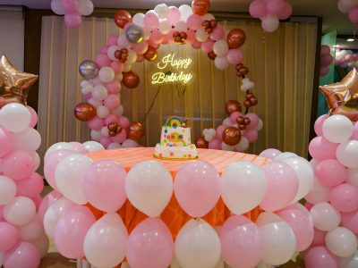 ibrant pink and white balloon arch with "Happy Birthday" neon sign and custom cake for a Valentine's Day themed birthday celebration.